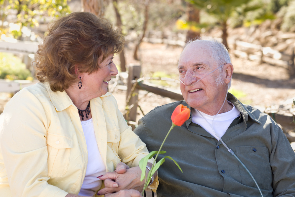 Senior,Woman,Outside,With,Seated,Man,Wearing,Oxygen,Tubes. elderly man receiving oxygen outside